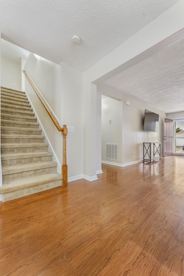 unfurnished living room with visible vents, a textured ceiling, wood finished floors, and stairs