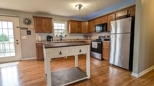 kitchen featuring tasteful backsplash, light wood-style flooring, appliances with stainless steel finishes, brown cabinets, and a sink