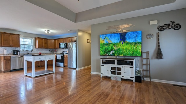 kitchen with baseboards, decorative backsplash, appliances with stainless steel finishes, wood finished floors, and a sink