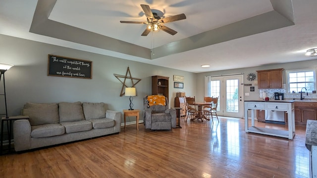 living area featuring a raised ceiling, wood finished floors, baseboards, and ceiling fan