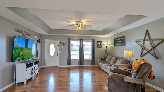 living area with baseboards, a raised ceiling, wood finished floors, and a ceiling fan