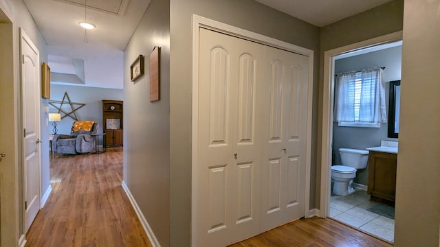 corridor featuring baseboards, attic access, and wood finished floors