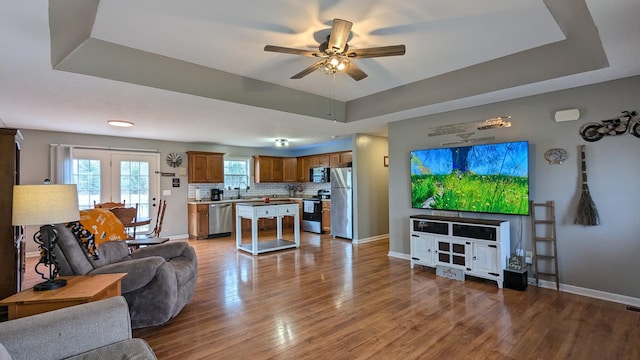 living room with a raised ceiling, wood finished floors, a ceiling fan, and baseboards