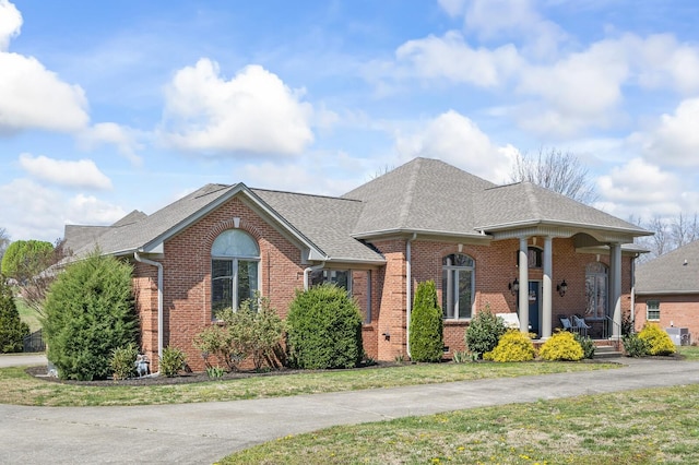 view of front of property with brick siding, a front yard, central air condition unit, and roof with shingles