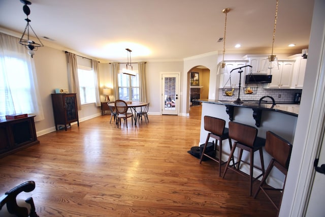 kitchen with a breakfast bar, backsplash, dark countertops, arched walkways, and white cabinets