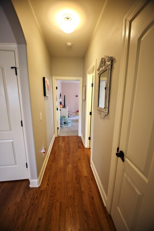 hall featuring arched walkways, dark wood-type flooring, and baseboards