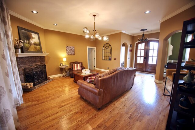living room featuring light wood-type flooring, arched walkways, a stone fireplace, baseboards, and a chandelier