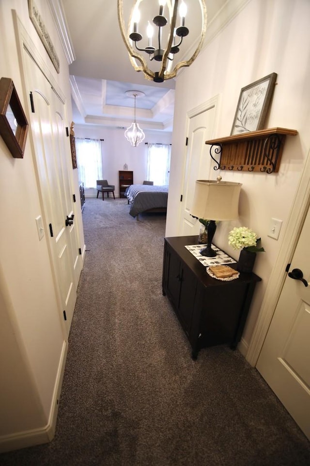 hall with baseboards, crown molding, a raised ceiling, dark carpet, and a chandelier