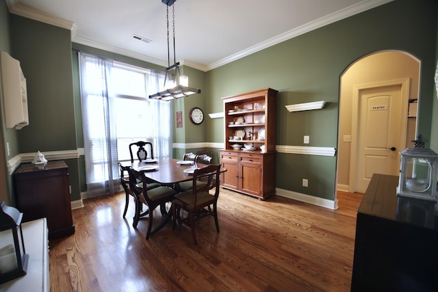 dining room featuring wood finished floors, visible vents, baseboards, arched walkways, and ornamental molding