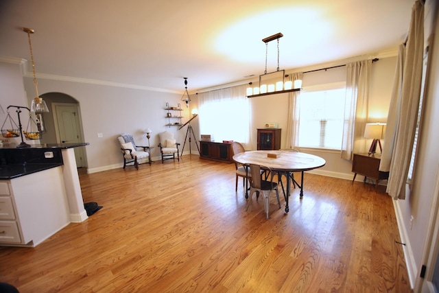 dining area featuring arched walkways, light wood-style floors, baseboards, and ornamental molding