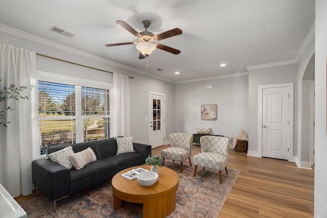 living room with wood finished floors, baseboards, visible vents, ornamental molding, and ceiling fan