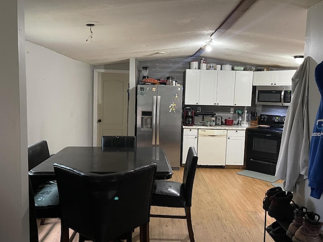 kitchen featuring light wood finished floors, vaulted ceiling, white cabinets, light countertops, and appliances with stainless steel finishes