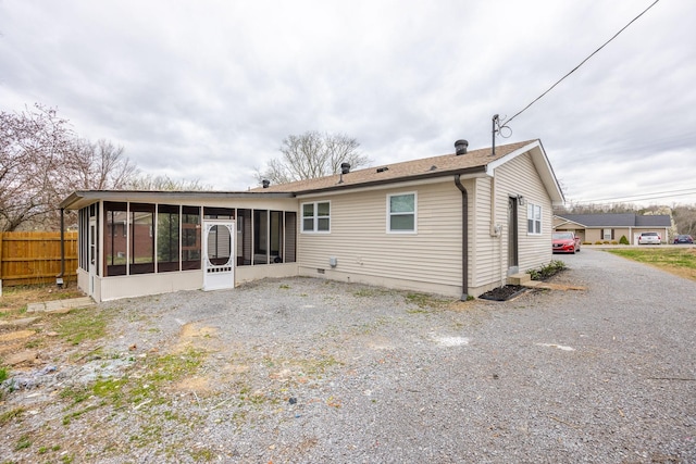 rear view of house with gravel driveway, a sunroom, and fence