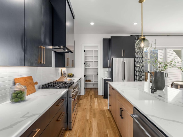 kitchen featuring backsplash, high end appliances, light wood-type flooring, a sink, and light stone counters