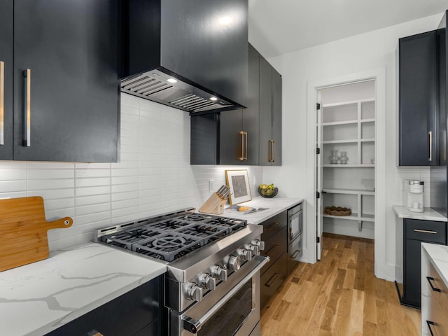kitchen with dark cabinets, decorative backsplash, stainless steel gas range, and light wood finished floors