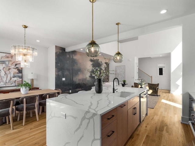 kitchen featuring light stone countertops, hanging light fixtures, a sink, dishwasher, and light wood-style flooring
