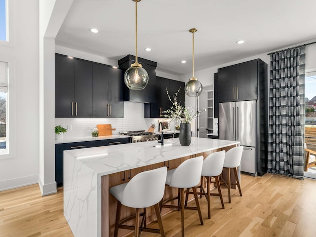 kitchen featuring decorative backsplash, light wood-type flooring, high end fridge, dark cabinets, and wall chimney exhaust hood