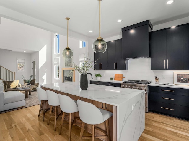 kitchen with dark cabinetry, light wood-style floors, stainless steel range, and wall chimney range hood