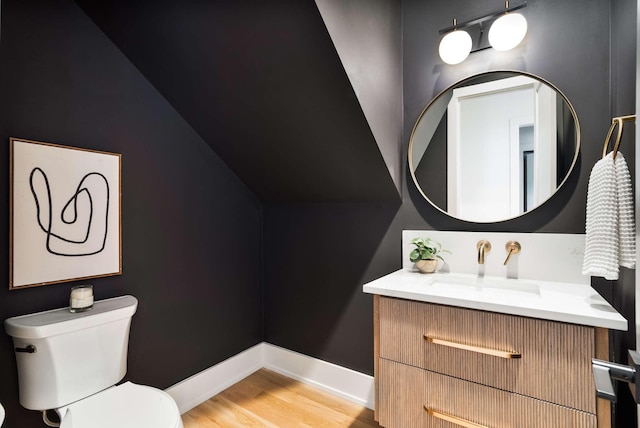bathroom with vanity, wood finished floors, toilet, baseboards, and vaulted ceiling