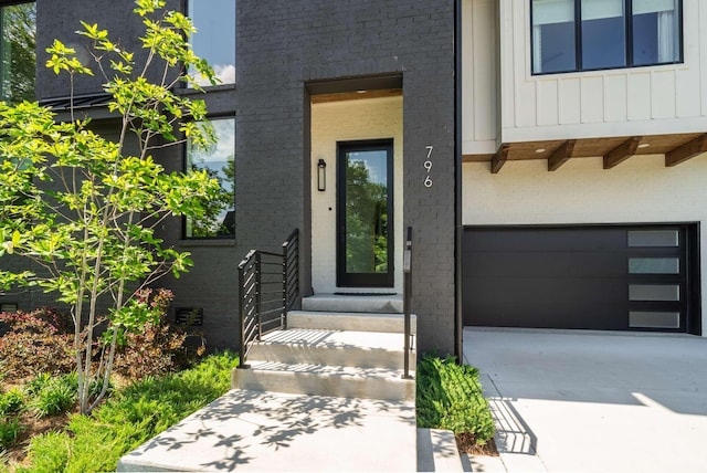 doorway to property featuring a garage, board and batten siding, driveway, and brick siding