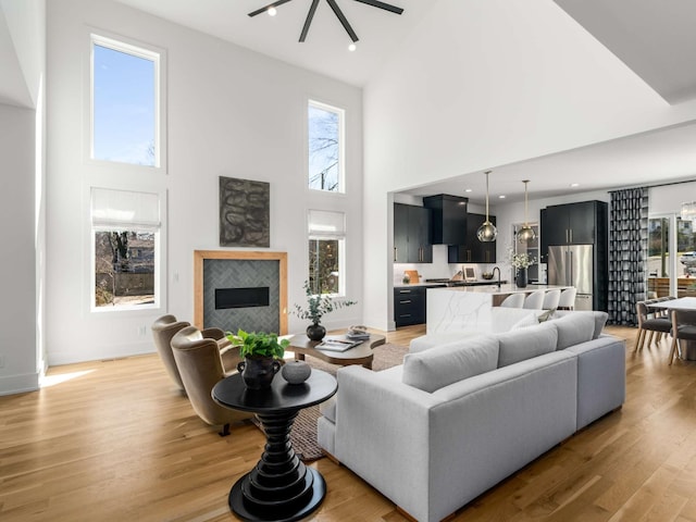 living area featuring a high ceiling, plenty of natural light, light wood-style floors, and a tile fireplace