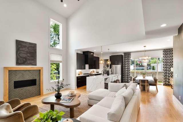 living area with a fireplace, high vaulted ceiling, a chandelier, recessed lighting, and light wood-type flooring