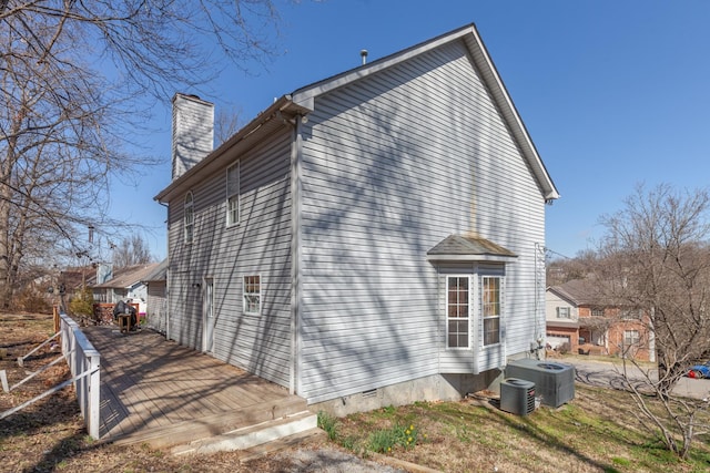 view of home's exterior featuring a wooden deck, a chimney, and central AC