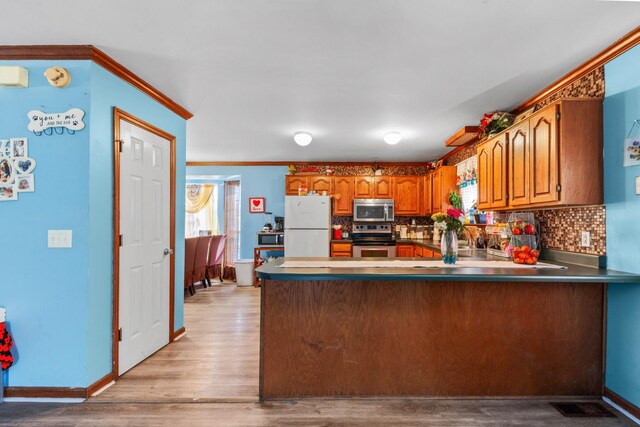 kitchen featuring brown cabinetry, backsplash, a peninsula, and stainless steel appliances