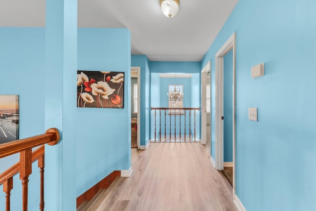 hall featuring wood finished floors, a notable chandelier, an upstairs landing, and baseboards