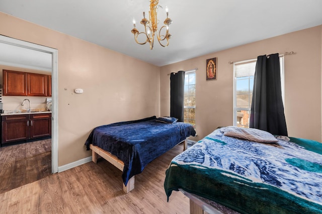 bedroom featuring a sink, baseboards, an inviting chandelier, and light wood-style flooring