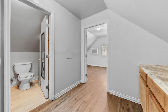 bathroom with toilet, lofted ceiling, an AC wall unit, wood finished floors, and baseboards