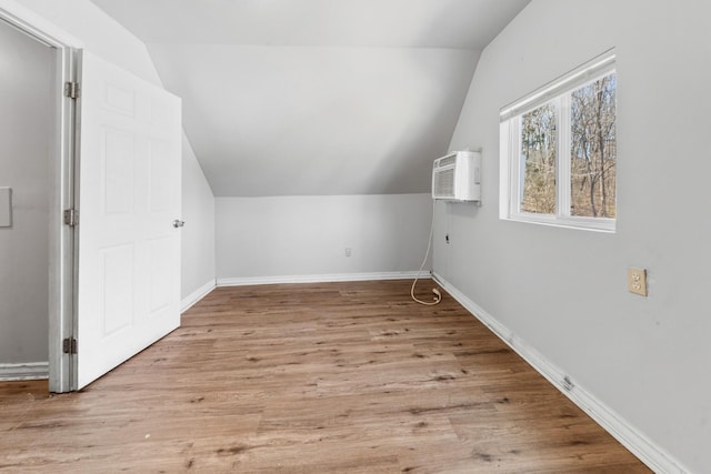 additional living space with baseboards, lofted ceiling, wood finished floors, and a wall mounted AC