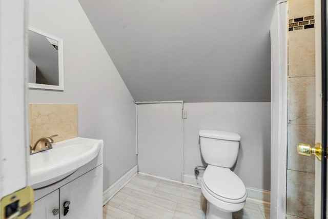 bathroom featuring vanity, lofted ceiling, toilet, and baseboards