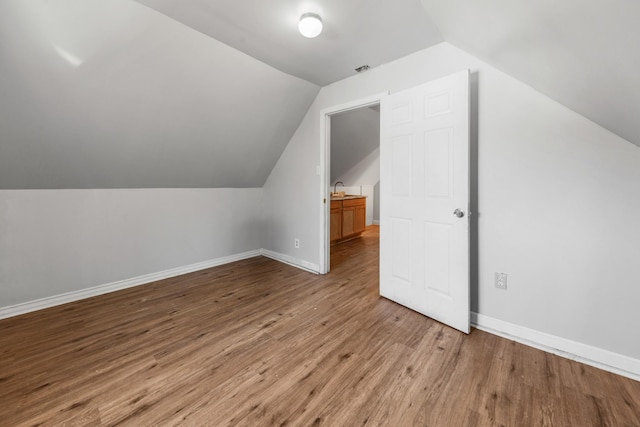 additional living space with a sink, baseboards, wood finished floors, and vaulted ceiling