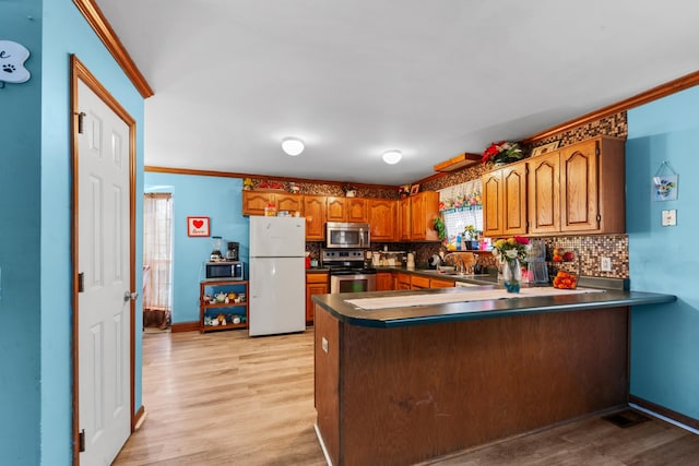 kitchen featuring brown cabinetry, a peninsula, stainless steel appliances, and light wood-type flooring