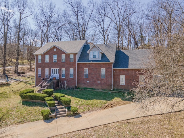 view of front facade with brick siding, a trampoline, a front yard, and a shingled roof