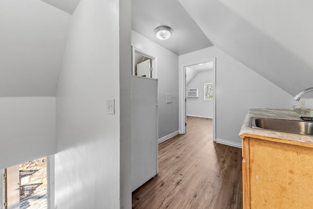 interior space with wood finished floors, baseboards, lofted ceiling, a sink, and a wall mounted air conditioner