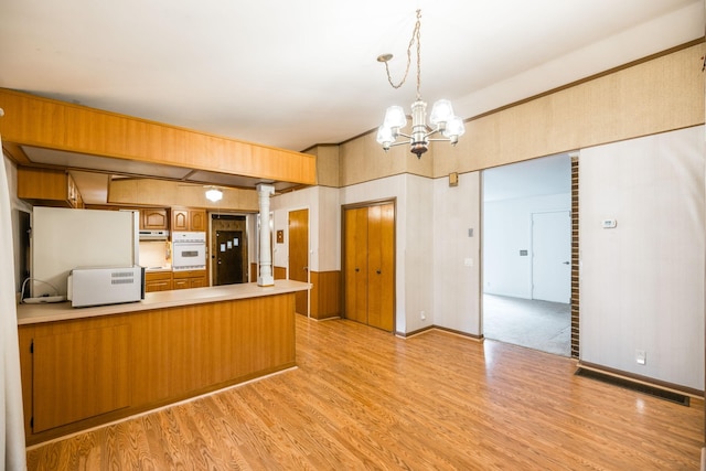 kitchen featuring light wood-style flooring, a peninsula, light countertops, and oven