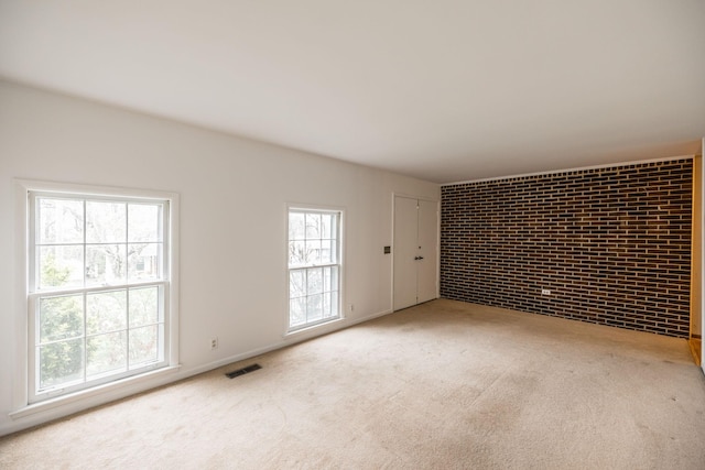 empty room featuring visible vents, carpet floors, and brick wall