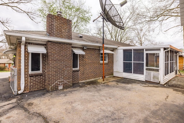 back of property featuring brick siding, a shingled roof, a chimney, and a sunroom