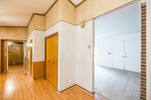 corridor with light carpet, light wood-type flooring, baseboards, and ornamental molding