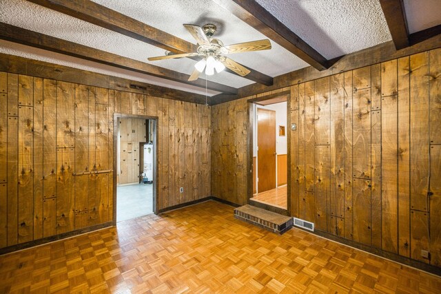 unfurnished room featuring baseboards, beam ceiling, a textured ceiling, and wood walls