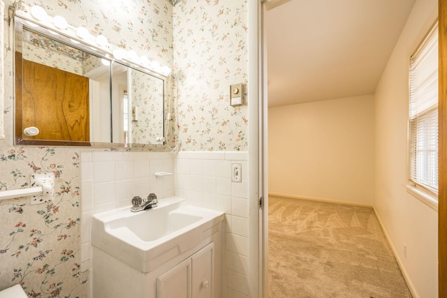 half bathroom featuring vanity, a wainscoted wall, baseboards, wallpapered walls, and tile walls