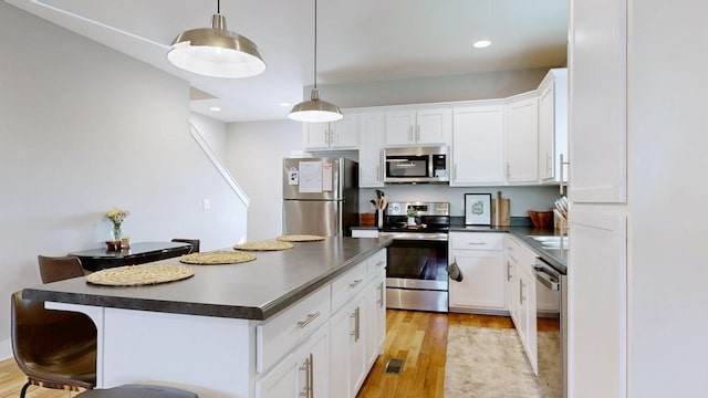 kitchen featuring dark countertops, a kitchen breakfast bar, stainless steel appliances, and light wood-type flooring