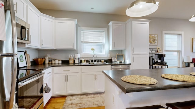 kitchen featuring a sink, stainless steel appliances, dark countertops, and a healthy amount of sunlight
