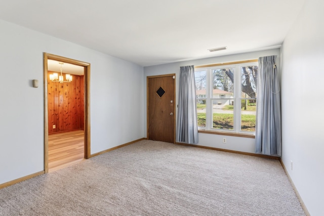 carpeted spare room with visible vents, baseboards, and an inviting chandelier