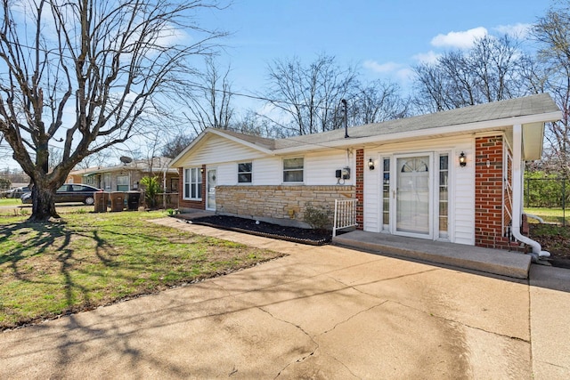 ranch-style home with brick siding, stone siding, a shingled roof, and a front lawn