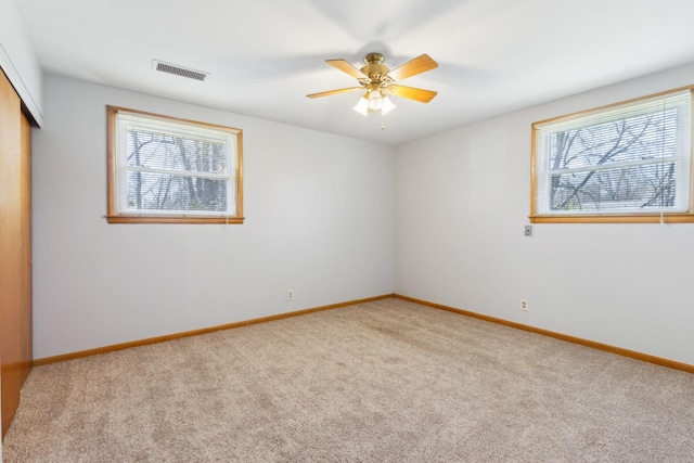 carpeted spare room featuring visible vents, baseboards, a healthy amount of sunlight, and a ceiling fan