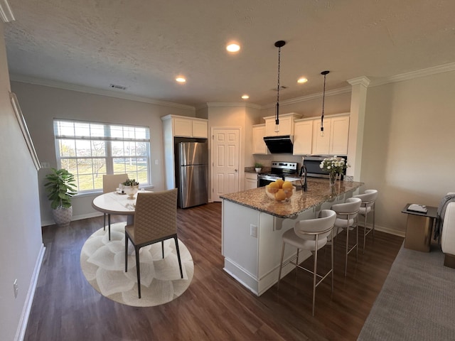 kitchen featuring dark wood finished floors, dark stone counters, a peninsula, appliances with stainless steel finishes, and white cabinets
