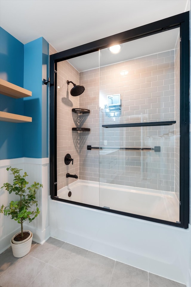 bathroom featuring tile patterned flooring, a wainscoted wall, and bath / shower combo with glass door